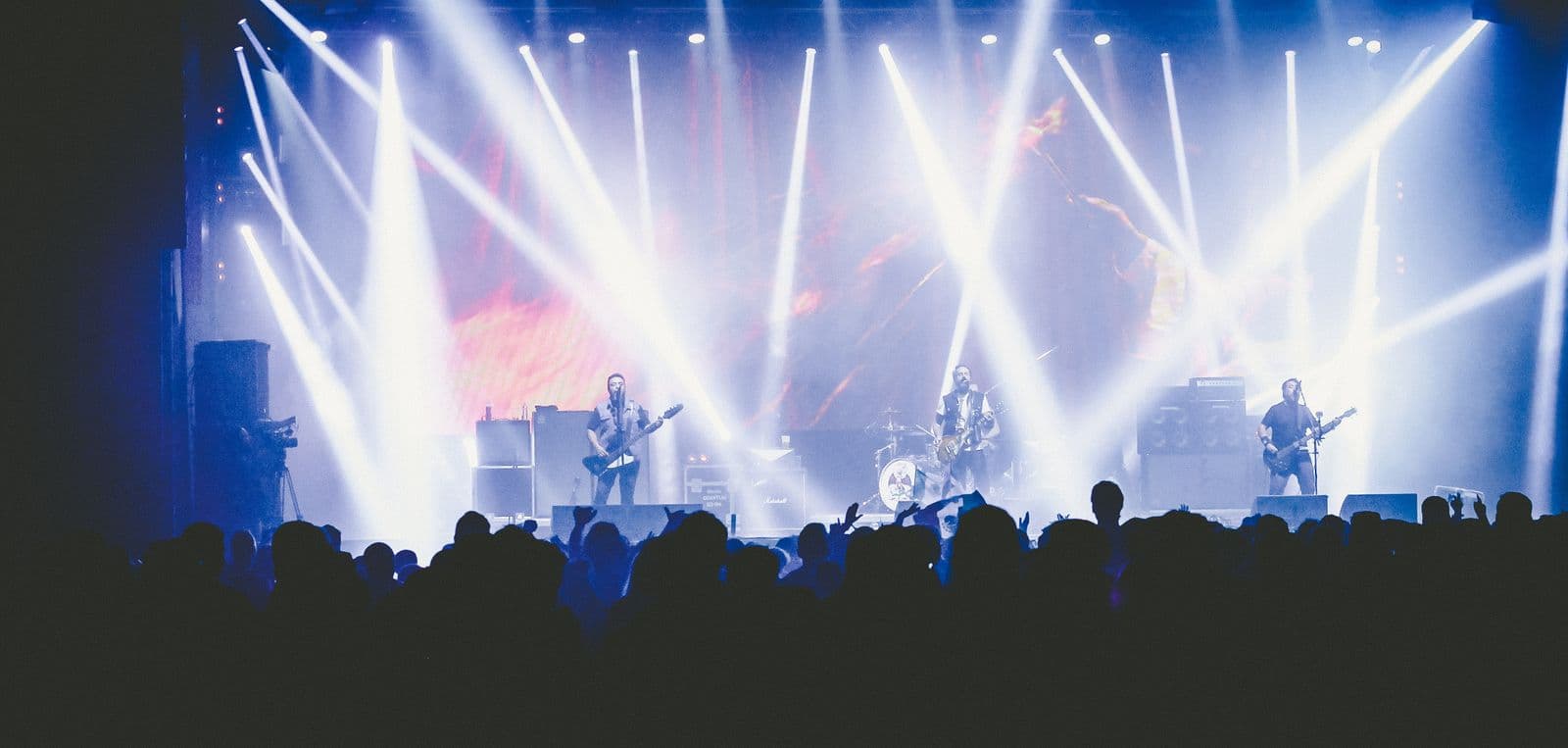 A crowd silhouetted against a live stage under sweeping lights